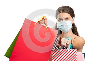 Woman wearing medical mask holding shopping bags pointing finger