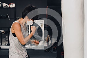 Woman wearing medical mask training boxing with punching bag in gym