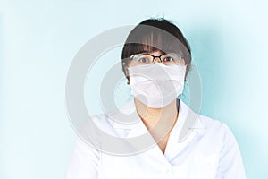 Woman is wearing a medical mask in a white uniform, protective blue gloves. Please stay at home. Copyspace
