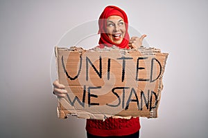 Woman wearing muslim hijab asking for union holding banner with united stand message pointing and showing with thumb up to the