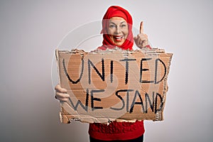 Woman wearing muslim hijab asking for union holding banner with united stand message surprised with an idea or question pointing