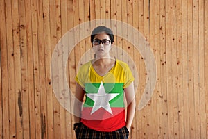 Woman wearing Myanmar flag color shirt and standing with two hands in pant pockets on the wooden wall background