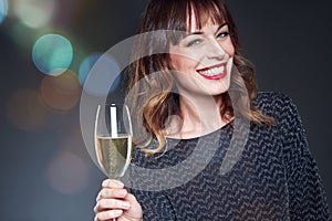 Woman wearing night party dress with a glass of champagne on dark background. Lady with long curly hair celebrating