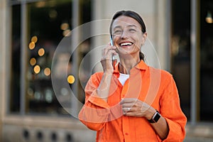 Woman wearing orange shirt standing in city street talking via mobile phone.