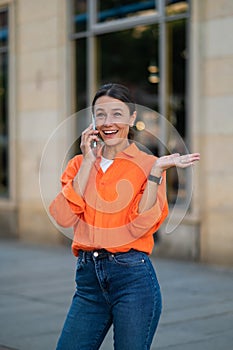 Woman wearing orange shirt standing in city street talking via mobile phone.