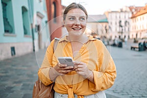 Woman wearing orange yellow shirt texting on the smart phone walking in the street in a sunny day