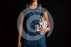 A woman wearing overalls holding a handmade rye bread wrapped with a cloth on a black background