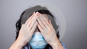 Woman wearing protection face mask against coronavirus covering her eyes with hands. Woman in a mask hiding her eyes