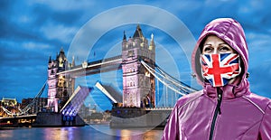 Woman wearing protection face mask with British flag against coronavirus in front of the Tower Bridge, London, England