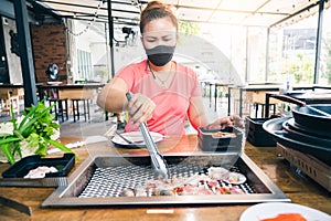 The woman wearing the protective face mask and grilling in the restaurant via the new normal method. the concept of coronavirus, n