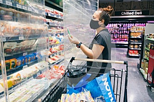 The woman wearing the protective face mask is shopping in the supermarket via the new normal method. the concept of the coronaviru