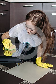 Woman, wearing in protective glove with rag cleaning oven at kitchen.