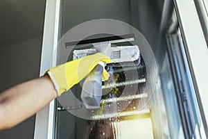 Woman wearing Protective Gloves Cleaning Window by spraying Cleaning Products and wiping with Sponge