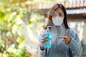 A woman wearing protective mask holding and pointing finger at a bottle of alcohol gel sanitizer for Healthcare