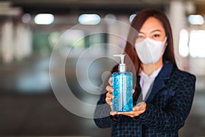 A woman wearing protective mask, holding and showing a bottle of alcohol gel sanitizer for Healthcare and Covid-