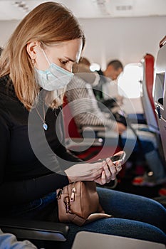 a woman wearing a protective mask reads sms on the phone on board the plane.