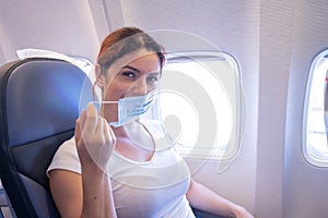A woman wearing a protective mask sits on the plane at the window.