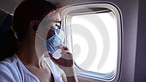 A woman wearing a protective mask sits on the plane at the window.