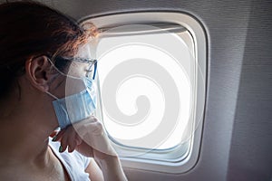 A woman wearing a protective mask sits on the plane at the window.