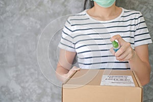 Woman wearing protective mask using spray alcohol sanitizer cleaning parcel post to prevent virus and bacterias from Postal sender