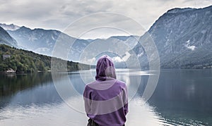 Woman wearing purple hoodie watching tranquil overcast morning scene at lake Bohinj, Alps mountains, Slovenia.