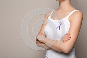 Woman wearing purple ribbon on grey background, closeup. Domestic violence awareness