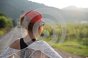 Woman wearing a red ballcap and a white lace shawl looks out on the rural landscape during the golden hour. Concept for dreaming,