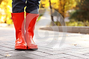 Woman wearing red rubber boots on paved street in park. Autumn walk