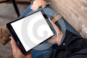 A woman wearing ripped jean sitting cross legged , holding black tablet pc with blank white desktop screen on thigh in cafe