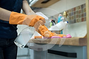 Woman wearing rubber gloves and cleaning the kitchen cabinets or surface