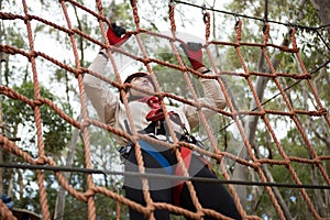 Woman wearing safety helmet climbing on a rope fence