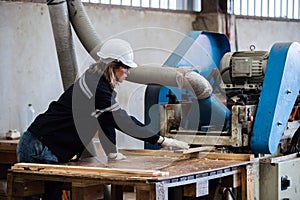 Woman wearing safety uniform and hard hat working on wood sanding electric machines at workshop manufacturing wooden. Female