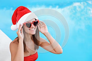 Young woman wearing Santa Claus hat near swimming pool. Christmas vacation