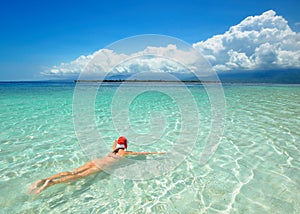 Woman is wearing Santa hat in bikini and swim in water at beach.
