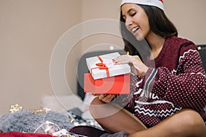 Woman wearing Santa hat opening gift in bed