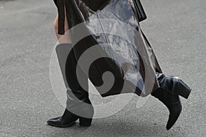 Woman wearing shiny dark brown coat, black handbag and boots