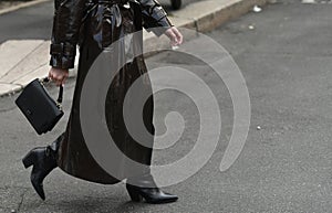 Woman wearing shiny dark brown coat, black handbag and boots