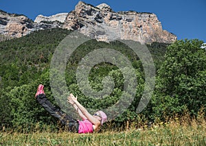 woman wearing sporty clothes, sunglasses and cap practicing relaxing yoga exercise or pilates in an idyllic place in front of a