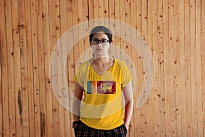 Woman wearing Sri Lanka flag color shirt and standing with two hands in pant pockets on the wooden wall background