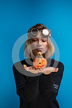 Woman wearing steampunk glasses and black hoodie holding a carved Halloween pumpkin