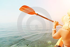 A woman wearing a straw hat is paddling a canoe on a sunny day. Scene is relaxed and carefree, as the woman enjoys her