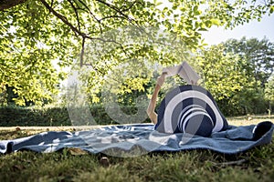 Woman wearing a straw hat in summer nature reading a book