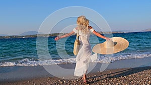 Woman wearing straw hat and white dress on shoreline at Spetses, Greece