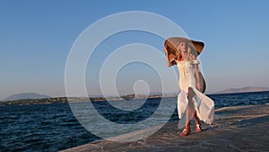 Woman wearing straw hat and white dress walking at embankment Spetses, Greece