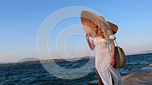 Woman wearing straw hat and white dress walking at embankment Spetses, Greece