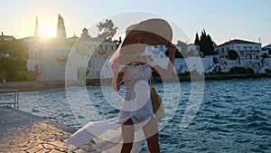 Woman wearing straw hat and white dress walking at embankment Spetses, Greece