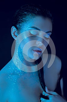 Woman wearing striking blue beauty makeup with glitter applied on her body