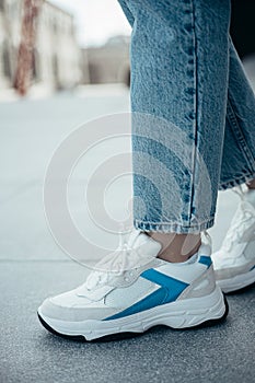 A woman wearing stylish sporty white sneakers on the street .Women`s sports shoes. Fashionable sneakers on female legs