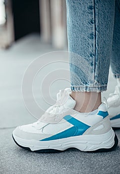 A woman wearing stylish white sneakers on the street .Women`s sports shoes. Fashionable sneakers on female legs. Close-up photo