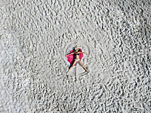 Woman wearing sun hat at the beach on white sand. Top view from drone. Aerial view of slim woman sunbathing lying on beach.